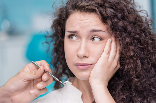 Woman holding cheek due to tooth ache before extractions at Calapooia Family Dental in Albany, OR